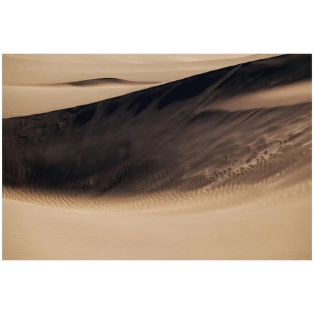 Aerial view of sand dunes showing contrasting dark shadows and light tan ripples across the desert terrain.