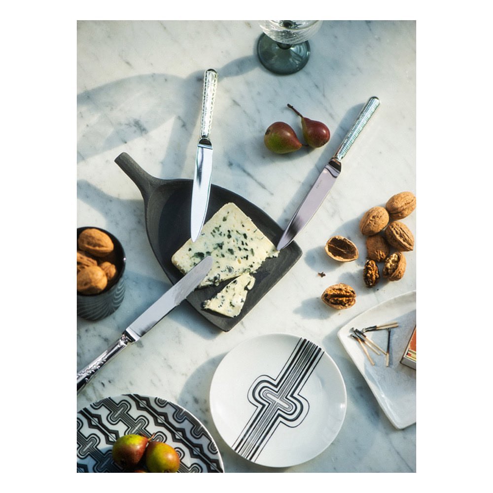 Overhead shot of a cheese board with blue cheese, pears, walnuts, ornate knives, decorative plates and glasses on a marble table.
