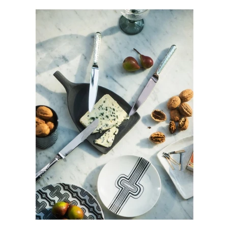 Overhead shot of a cheese board with blue cheese, pears, walnuts, ornate knives, decorative plates and glasses on a marble table.