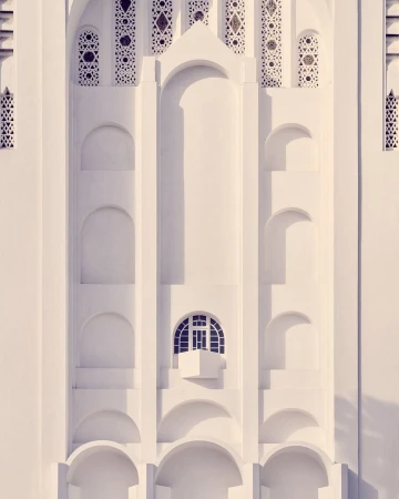 Architectural detail of an ornate white building facade with arched openings and a small window, showcasing intricate design and symmetry.