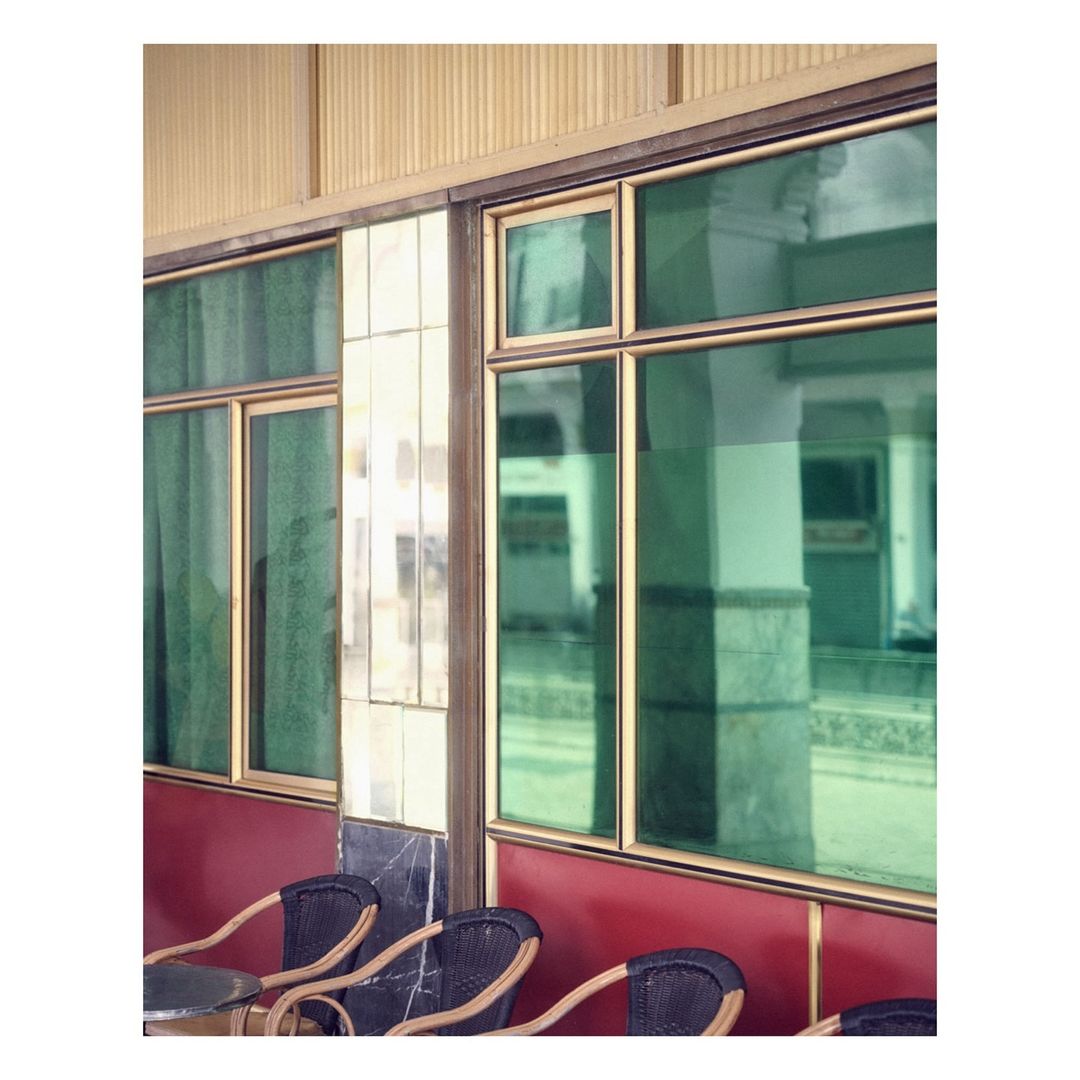 Exterior cafe view with green-tinted windows, wicker chairs, cream and marble paneling, creating a vintage, tranquil ambiance.