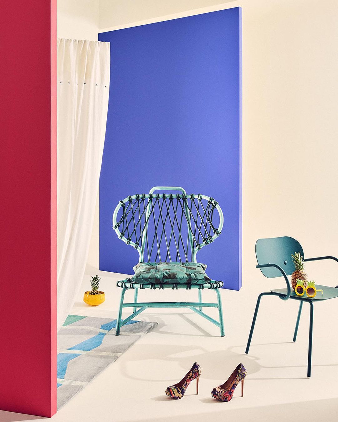 Colorful interior scene featuring light blue chairs, high heels, and a rug on a beige floor against a backdrop of pink, white, and blue panels.