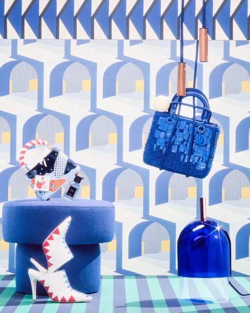Eye-level shot of a blue purse, decorative shoes, and a blue glass container against a patterned backdrop. Studio product shot.