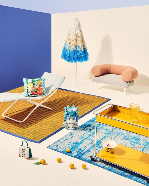 Still life composition featuring a designer beach umbrella, lounge chair, and colorful decorative objects arranged in a studio setting.