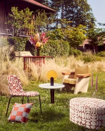 Outdoor lounge furniture set up on a grassy lawn with patterned seating and a small table with floral arrangements.