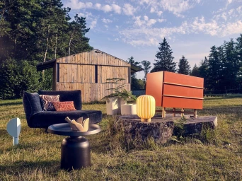 Modern outdoor furniture set featuring a navy armchair, orange cabinet, and yellow striped lamp in a grassy field.