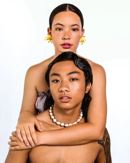 Close-up of two Asian people, one wearing yellow floral earrings and the other wearing a pearl necklace against a white backdrop.