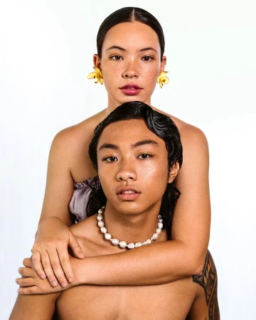 Close-up of two Asian people, one wearing yellow floral earrings and the other wearing a pearl necklace against a white backdrop.