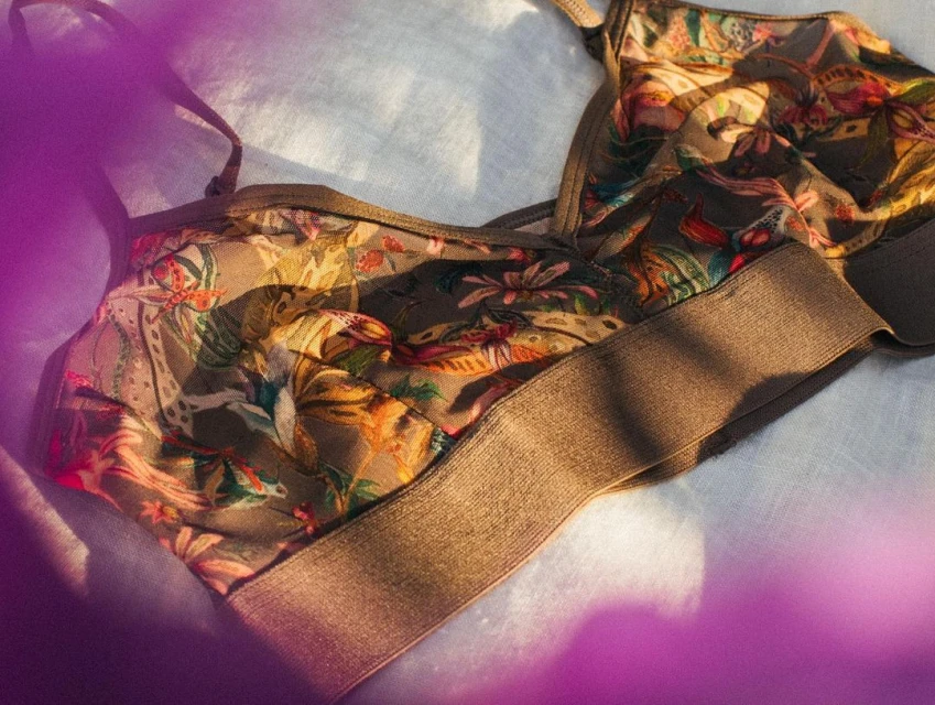 Floral-patterned lingerie bra top lies on a light blue textured surface with soft lighting, creating a fashion product still life.