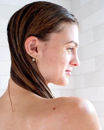 Profile portrait of a woman with wet brown hair and droplets on her skin against a tiled wall