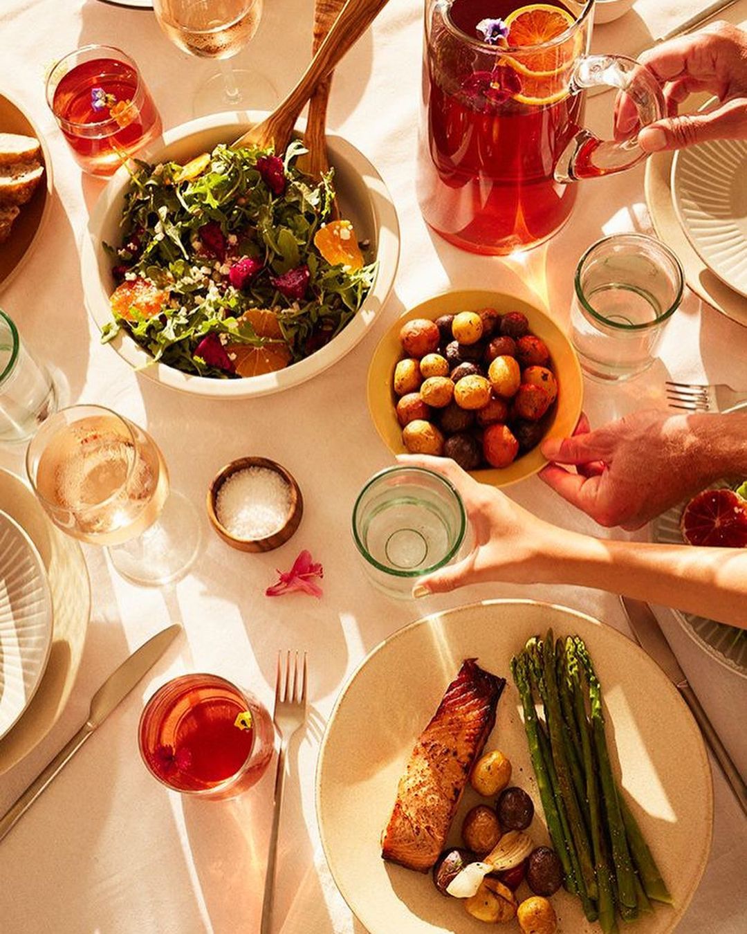 Overhead shot of a table set with salad, salmon, potatoes, drinks, and flatware creating a vibrant and inviting dining scene.