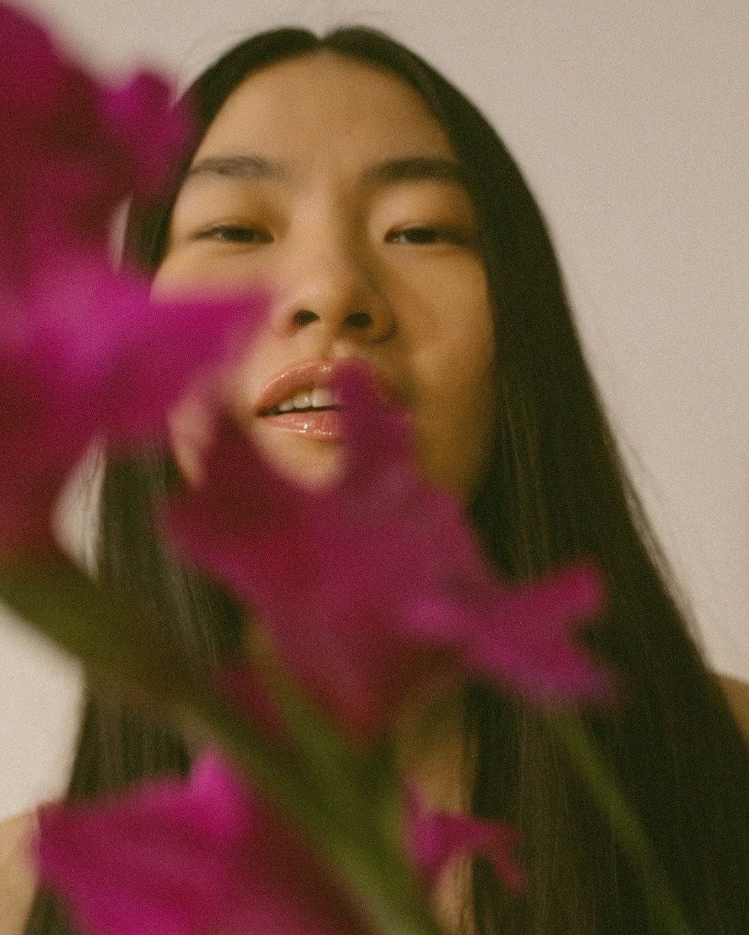 Close-up portrait of a woman partially obscured by vibrant magenta flowers in the foreground, photographed by Daeja Fallas.