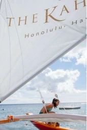 Woman in bikini on a catamaran sailboat with a branded sail reading The Kahala Honolulu Hawaii