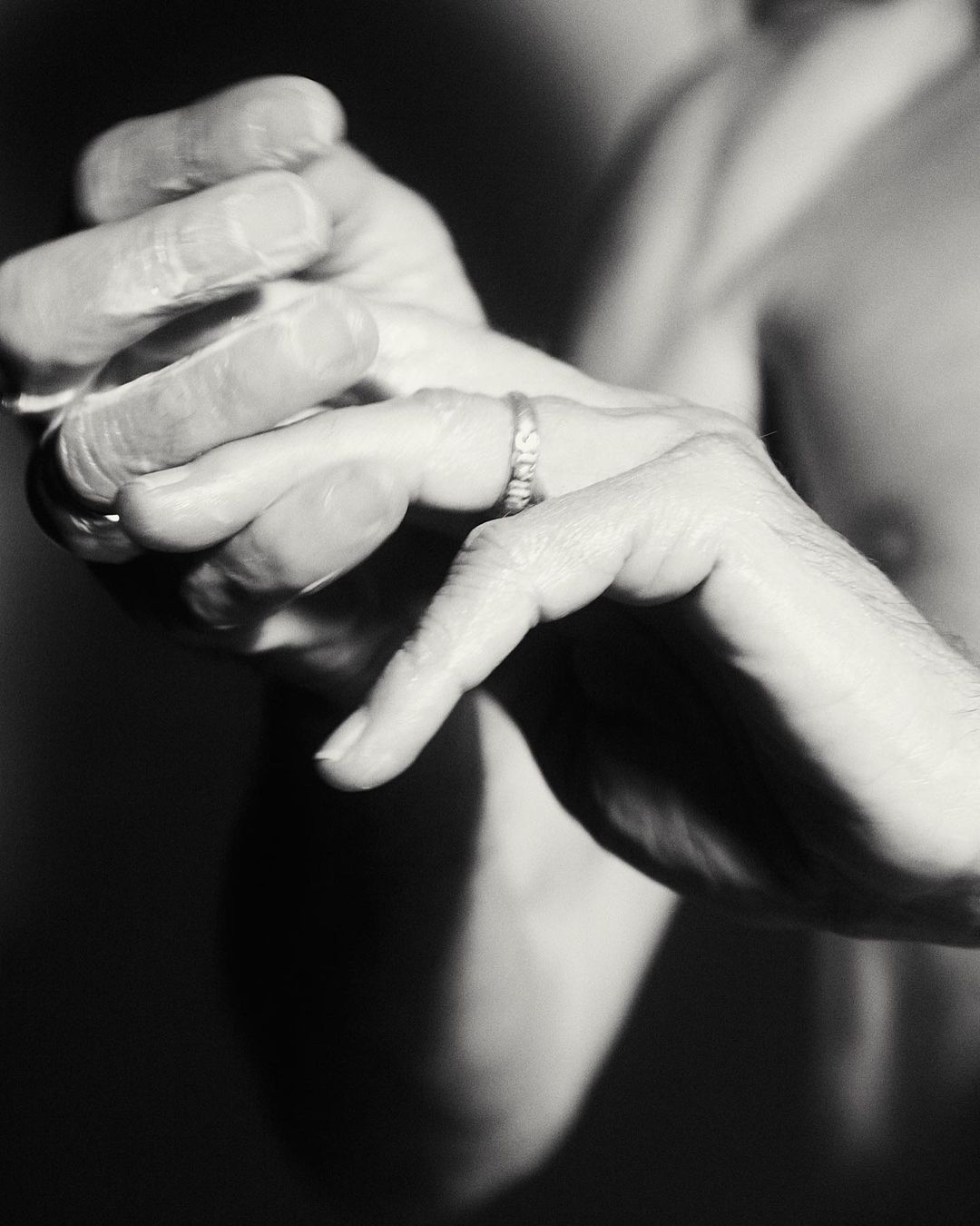 Close-up studio shot of an adult male's hands, one adorned with a wedding ring, against a dark backdrop, emphasizing texture and detail.