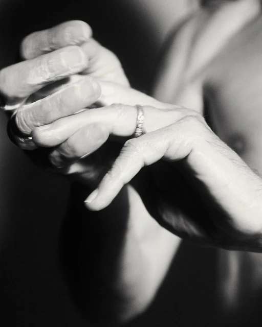 Close-up studio shot of an adult male's hands, one adorned with a wedding ring, against a dark backdrop, emphasizing texture and detail.