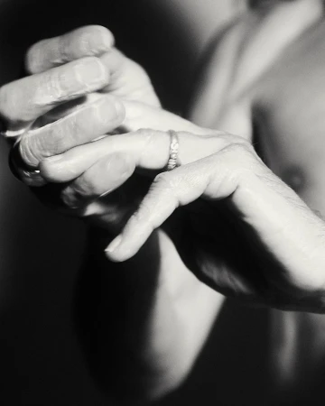 Close-up studio shot of an adult male's hands, one adorned with a wedding ring, against a dark backdrop, emphasizing texture and detail.