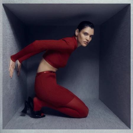 Model in red turtleneck and red trousers kneeling inside a grey cubic set by Daisy Walker