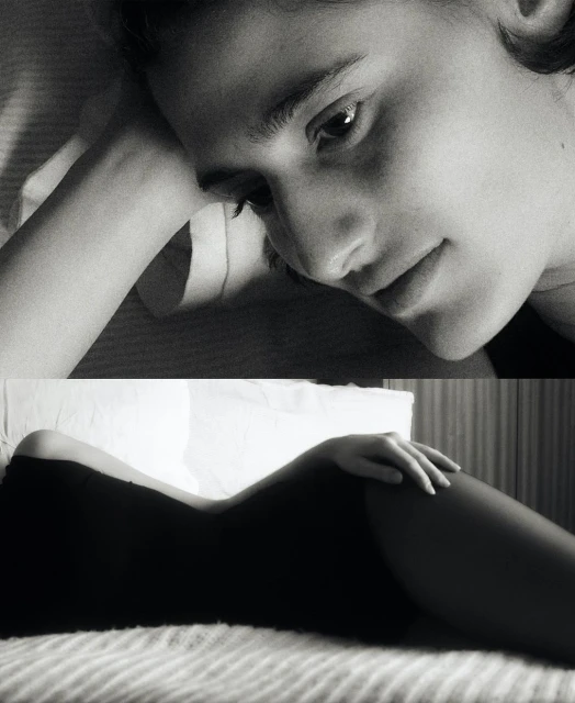 Monochrome portrait of a young woman lying in bed with her head resting on her arm, eyes looking towards the viewer. 