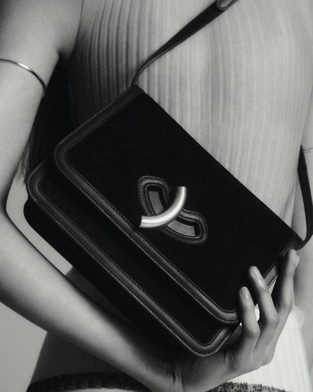Black velvet handbag with a silver clasp held by an adult woman in a monochromatic, close-up fashion shot.