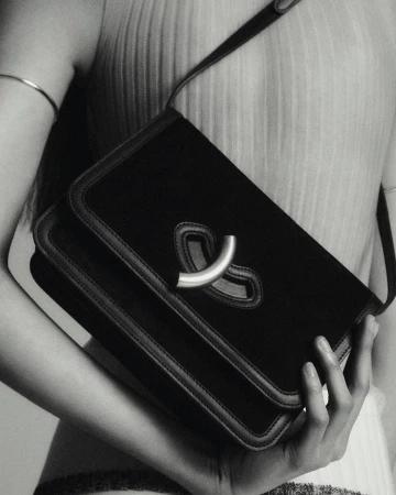 Black velvet handbag with a silver clasp held by an adult woman in a monochromatic, close-up fashion shot.