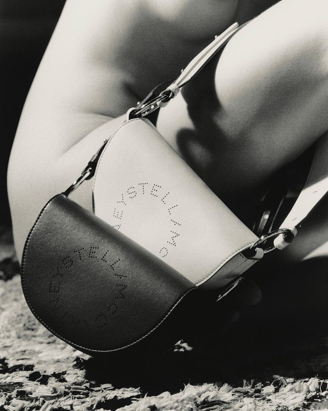 Close-up of a Stella McCartney half-moon purse with logo against a backdrop of textured material, presented in black and white.