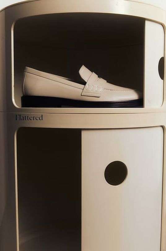 Cream-colored leather loafer inside of a round cabinet with black sole, spotlighting fashion footwear within a minimalist indoor setting.