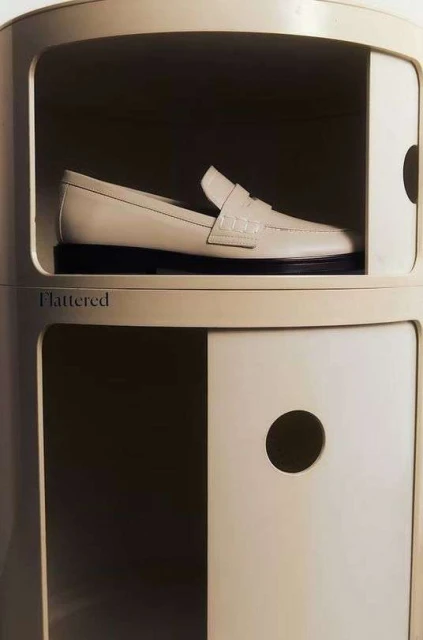Cream-colored leather loafer inside of a round cabinet with black sole, spotlighting fashion footwear within a minimalist indoor setting.