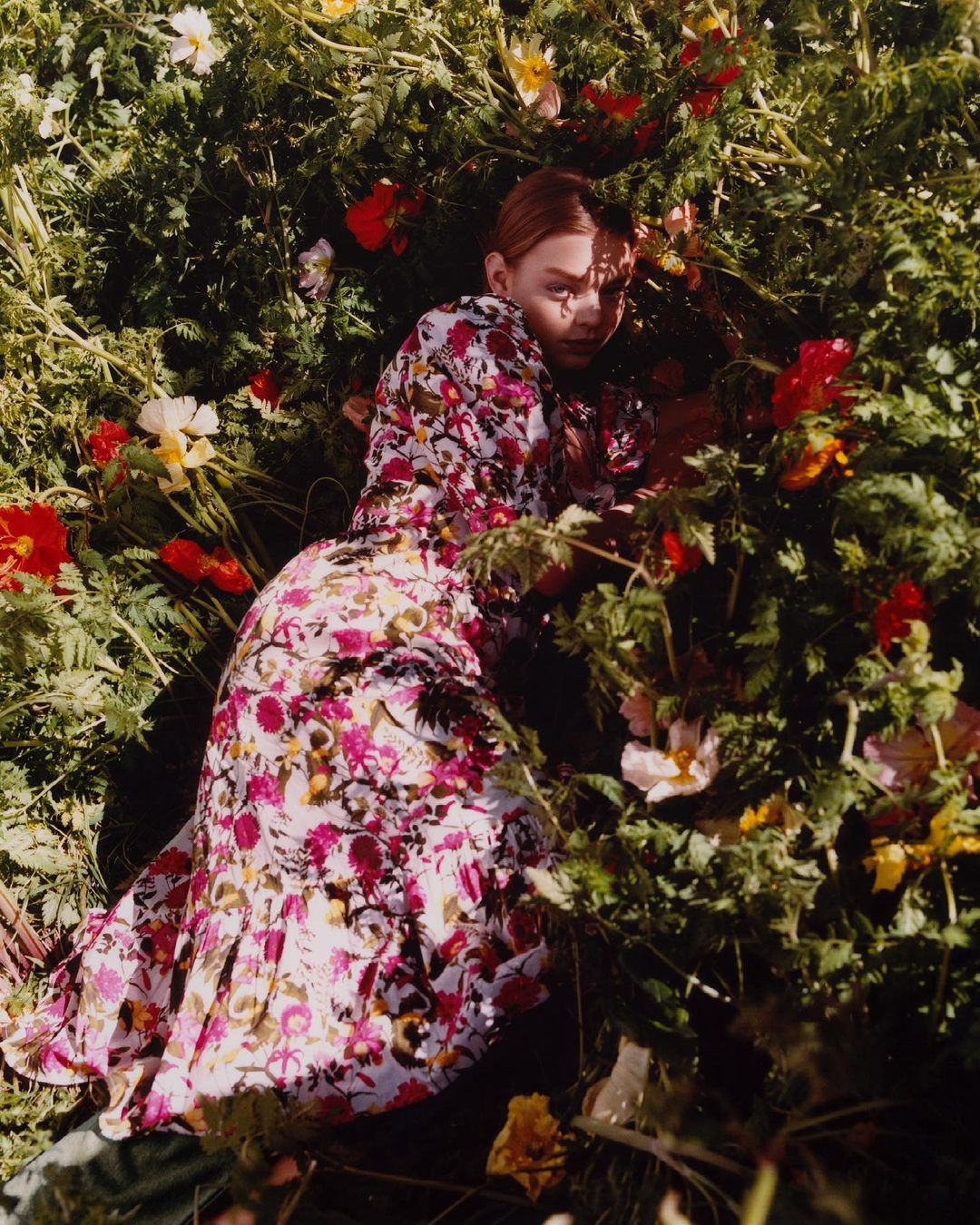 A woman in a floral dress lying in a field of wildflowers, creating a vibrant and natural portrait with a focus on nature and beauty.