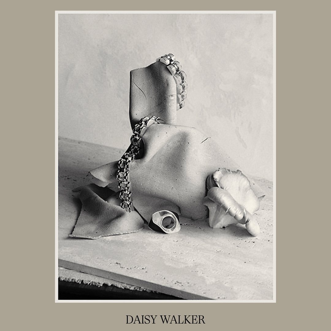 Still life featuring jewelry on a mannequin fragment, set against a neutral backdrop, exhibiting textures and a muted monochrome palette.