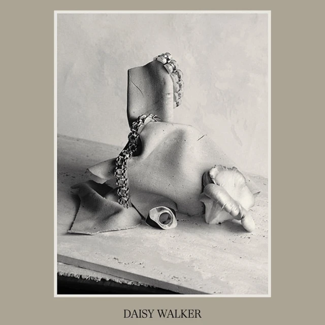 Still life featuring jewelry on a mannequin fragment, set against a neutral backdrop, exhibiting textures and a muted monochrome palette.