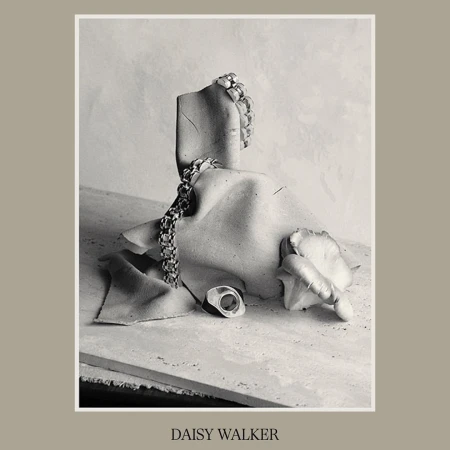 Still life featuring jewelry on a mannequin fragment, set against a neutral backdrop, exhibiting textures and a muted monochrome palette.