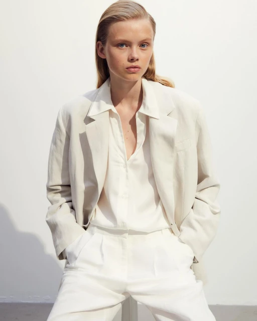 Fashion portrait of a blonde woman wearing an oversized linen blazer and trousers, set against a neutral background in a studio environment.