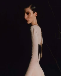 Portrait of a woman with dark short hair wearing a cream long-sleeve top against a dark background