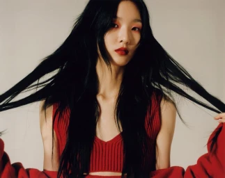 Woman with long black hair holding strands up, wearing red sleeveless top against light background
