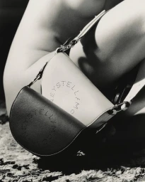 Close-up black and white editorial photograph of two curved leather handbags resting against a human figure.