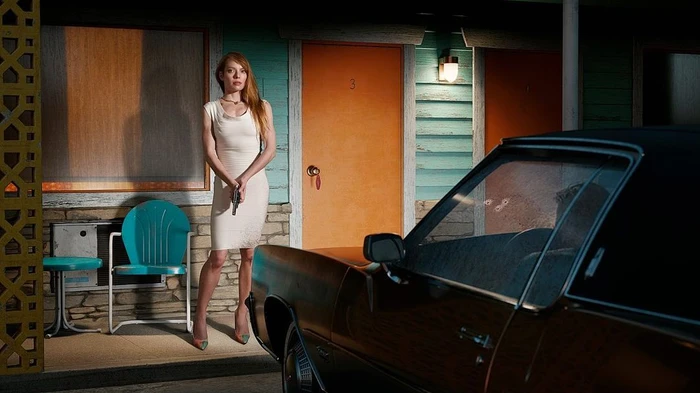 Woman in white dress holding a handgun standing outside a motel room next to a car