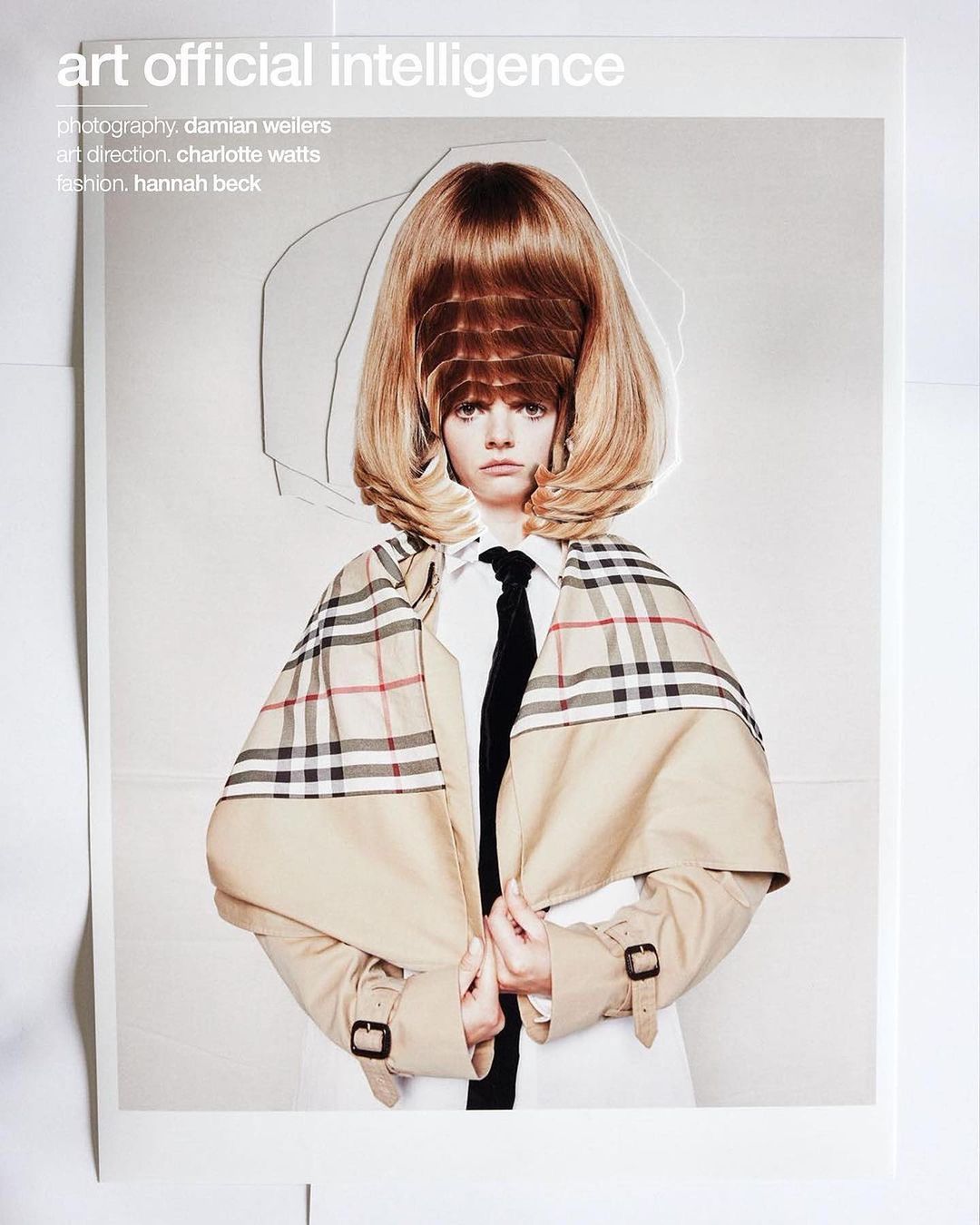 Fashion editorial featuring a woman with a distinctive hairstyle wearing a Burberry trench coat, white shirt, and black tie, against a light background.