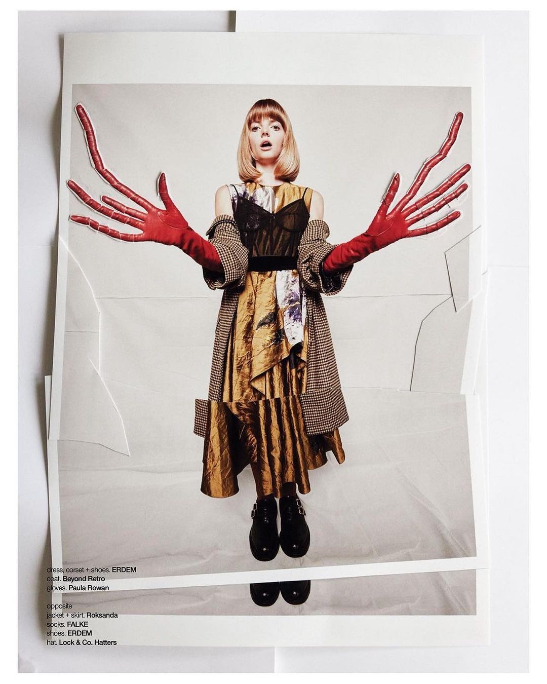A fair-skinned woman with blonde hair poses in a print, wearing a dress with red gloves, against a light backdrop with textured paper.