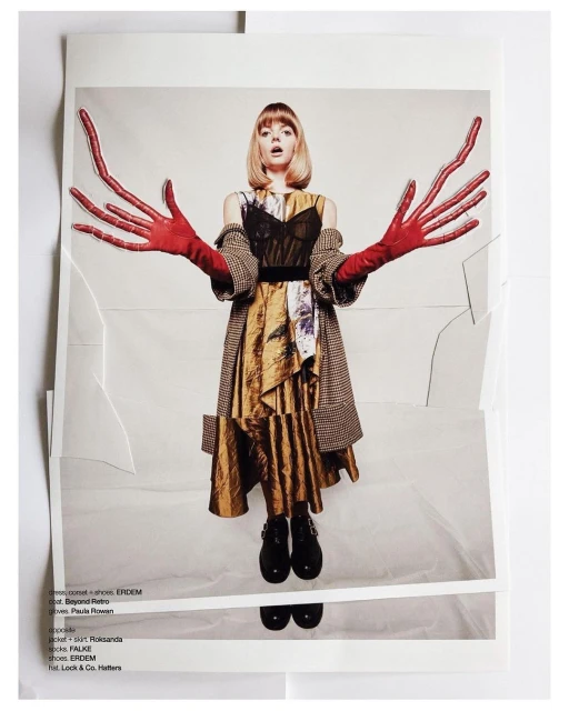 A fair-skinned woman with blonde hair poses in a print, wearing a dress with red gloves, against a light backdrop with textured paper.