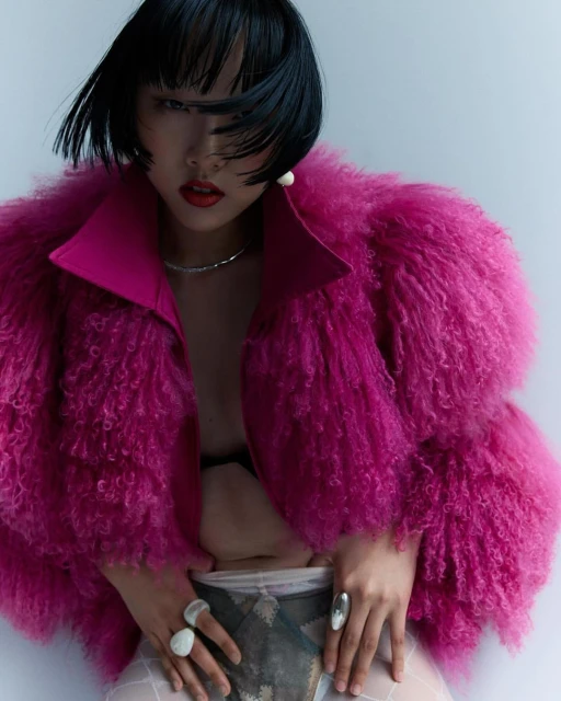 Portrait of a stylish Asian woman in a bright pink fur coat against a white background, showcasing fashion, beauty, and modern style.