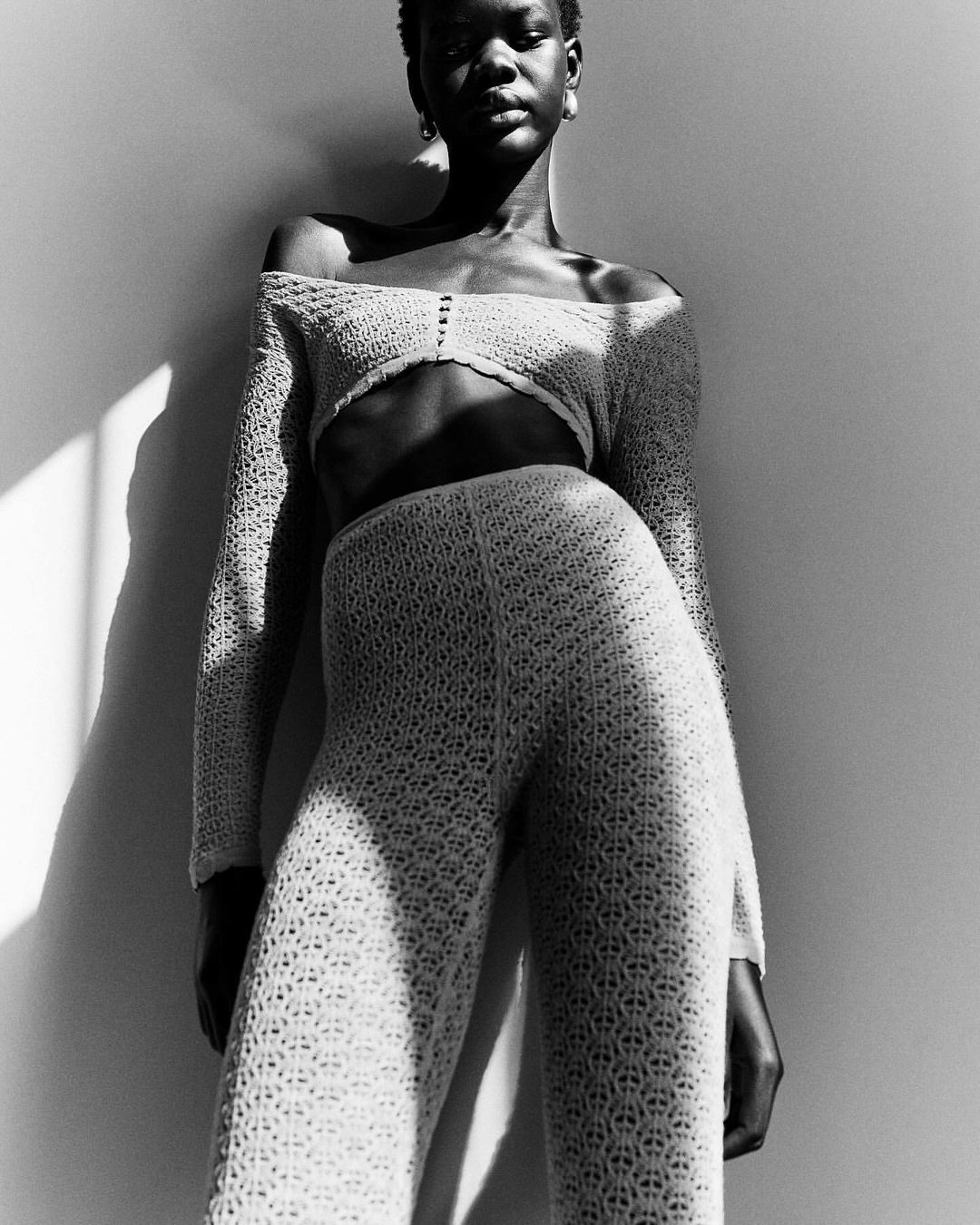 Model in off-the-shoulder knit top and matching pants photographed in dramatic high-contrast lighting by Damian Weilers.
