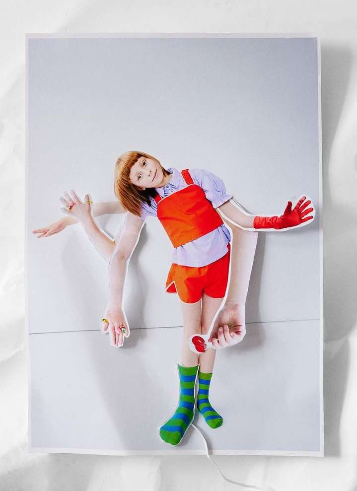 Young girl in red shorts and a matching vest poses in a studio with multiple arms created via collage art, showcasing a playful fashion concept.