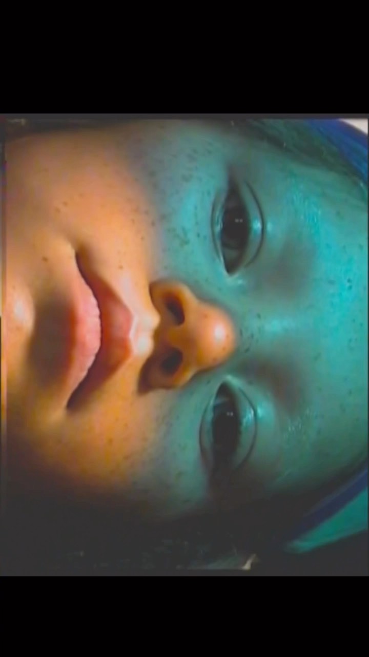 Close-up of a doll's face, featuring its eyes, nose, and mouth, bathed in blue and yellow lighting, with selective focus and shallow depth of field.