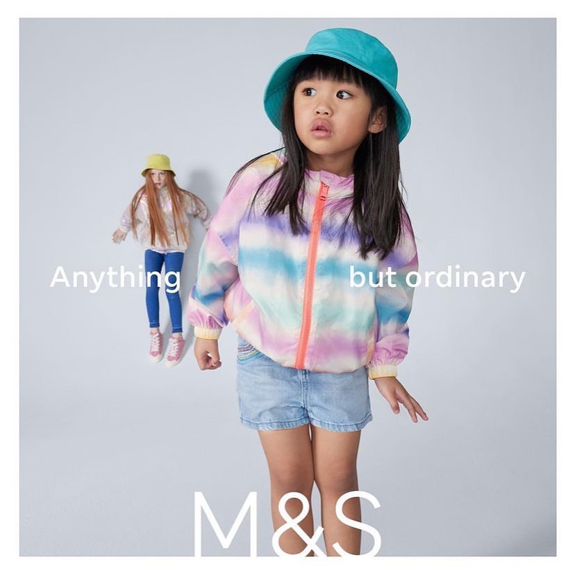 Two young girls in a studio setting modelling clothing from Marks and Spencer; one is wearing a colorful jacket and shorts.