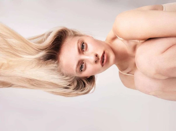 Portrait of a blonde woman with long hair and neutral makeup posing against a plain white background by Damian Weilers