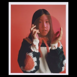 Young woman holding a translucent pink disk in front of her face against a solid red background