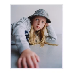 Young girl with freckles wearing a patterned bucket hat and grey sweatshirt resting on a grey surface