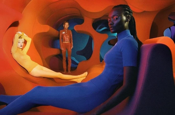 Three women in colorful outfits pose in a futuristic orange and blue tunnel setting, showcasing fashion and style in a studio environment.