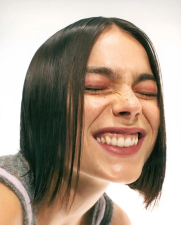 Close up portrait of a woman with short dark hair squinting and smiling against a white background