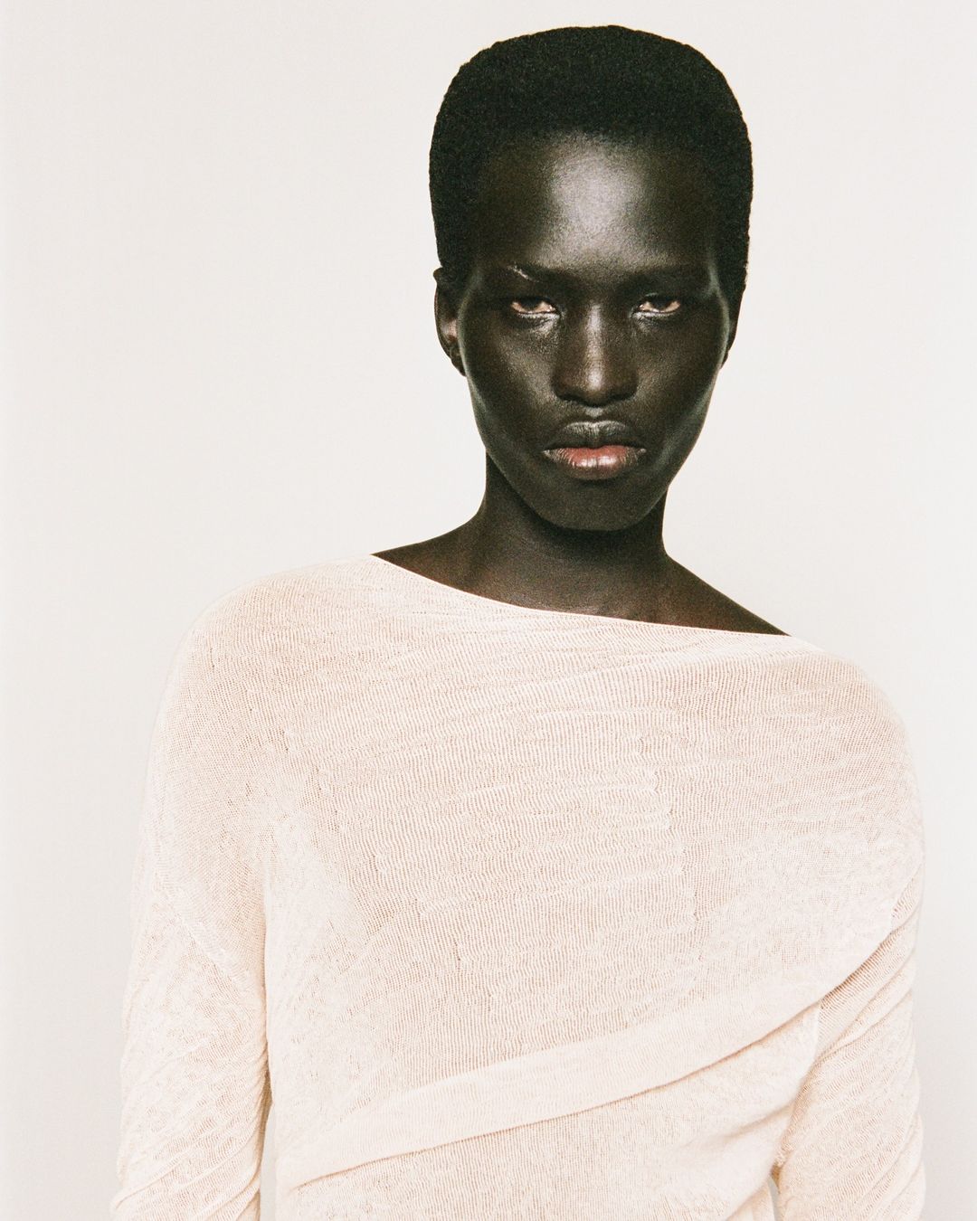 Portrait of a Black man wearing a textured light-colored top against a plain white background by Damien Krisl.